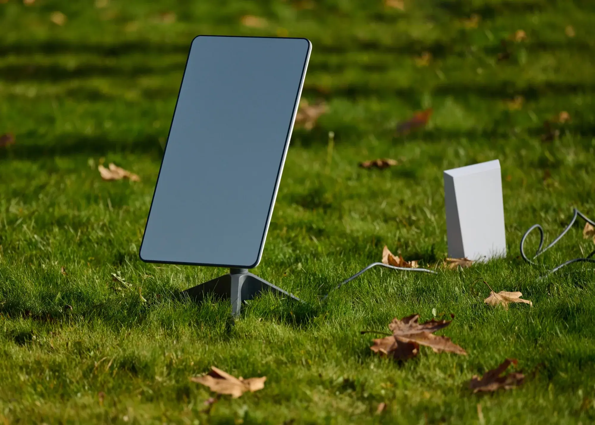 Starlink satellite dish on a tripod stand in a grassy yard beside its router - photo